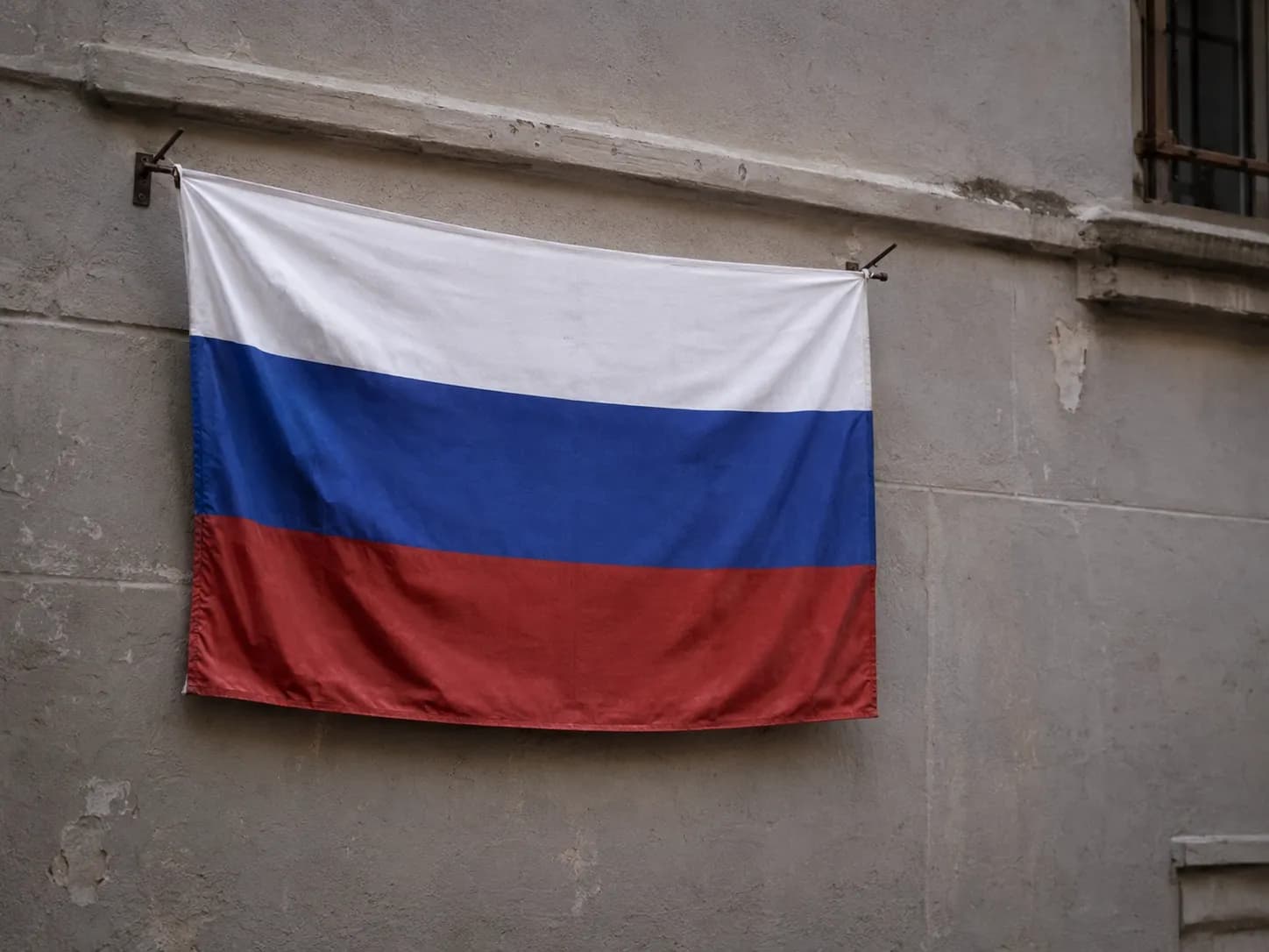 Russian tricolour flag hanging on brackets against a weathered stone wall