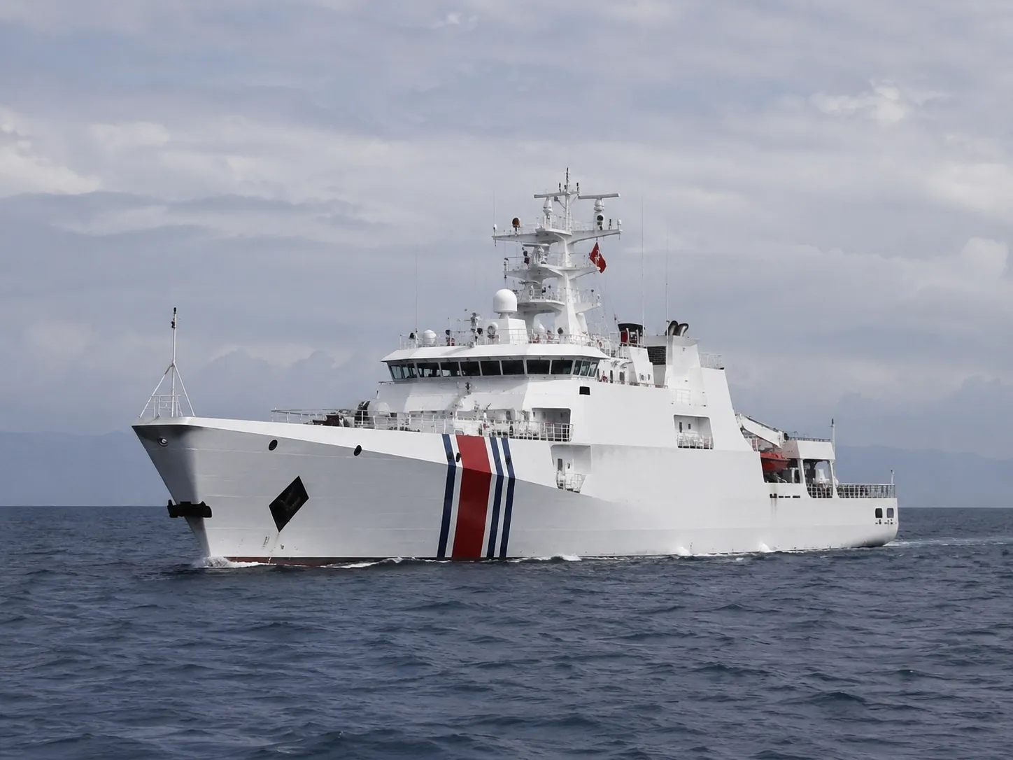 White coast guard patrol ship with red and blue stripes cutting through open water
