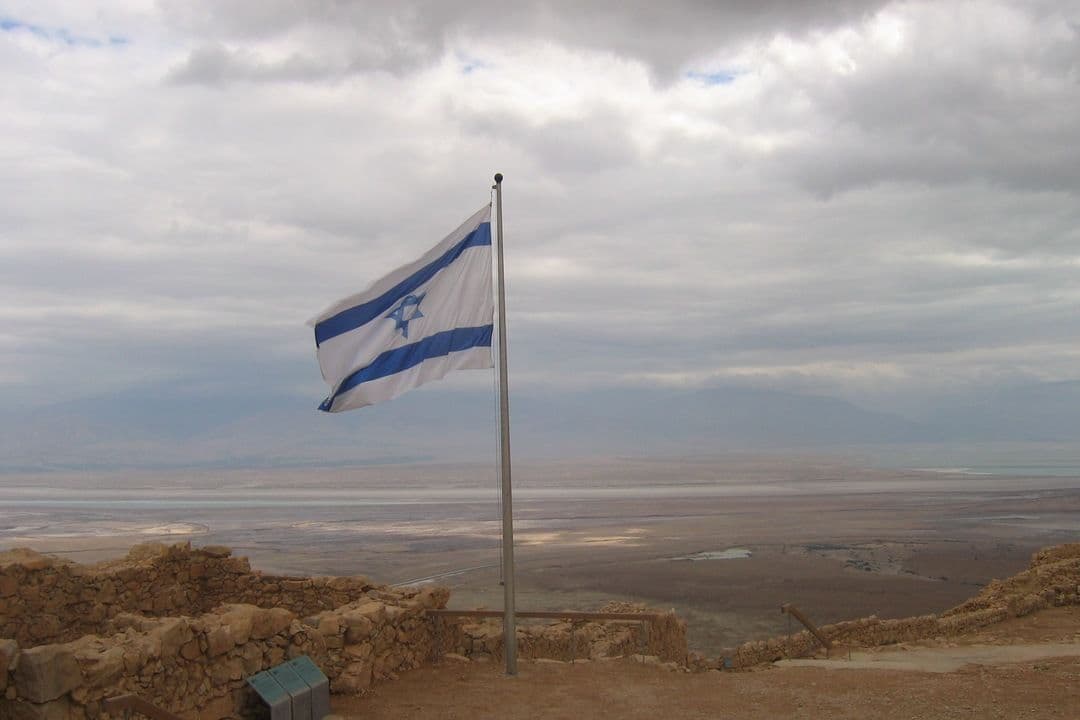 Israeli flag flying over ancient ruins with desert valley beyond