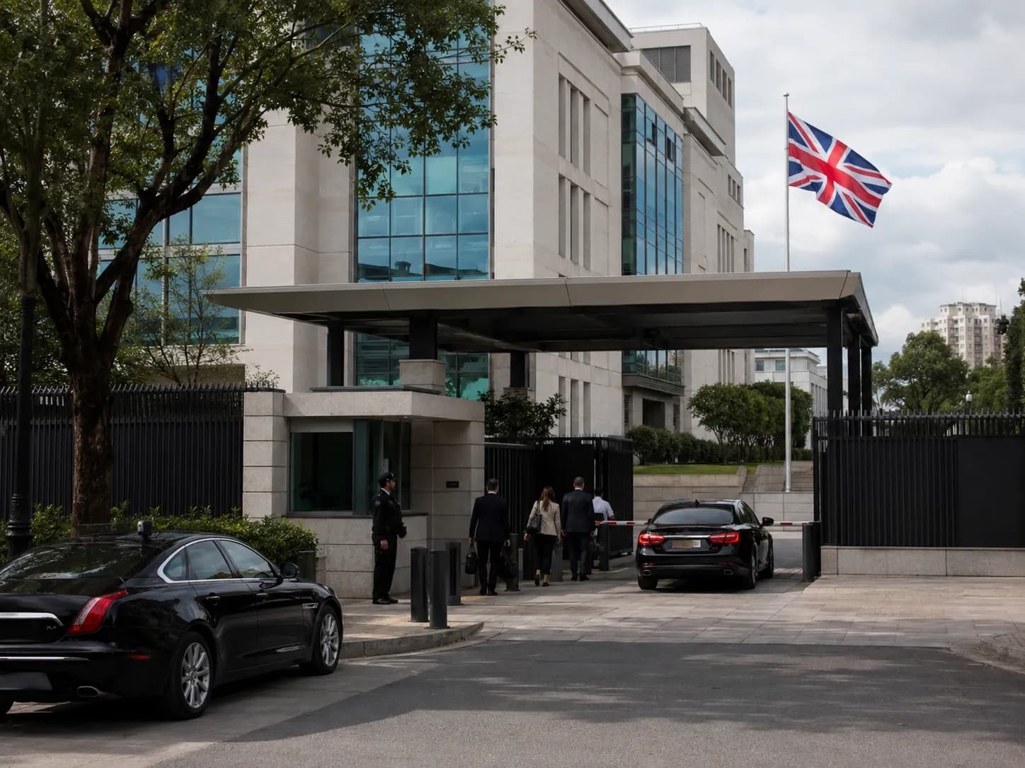 Visitors enter a modern British embassy compound abroad, Union Jack flying at half-mast