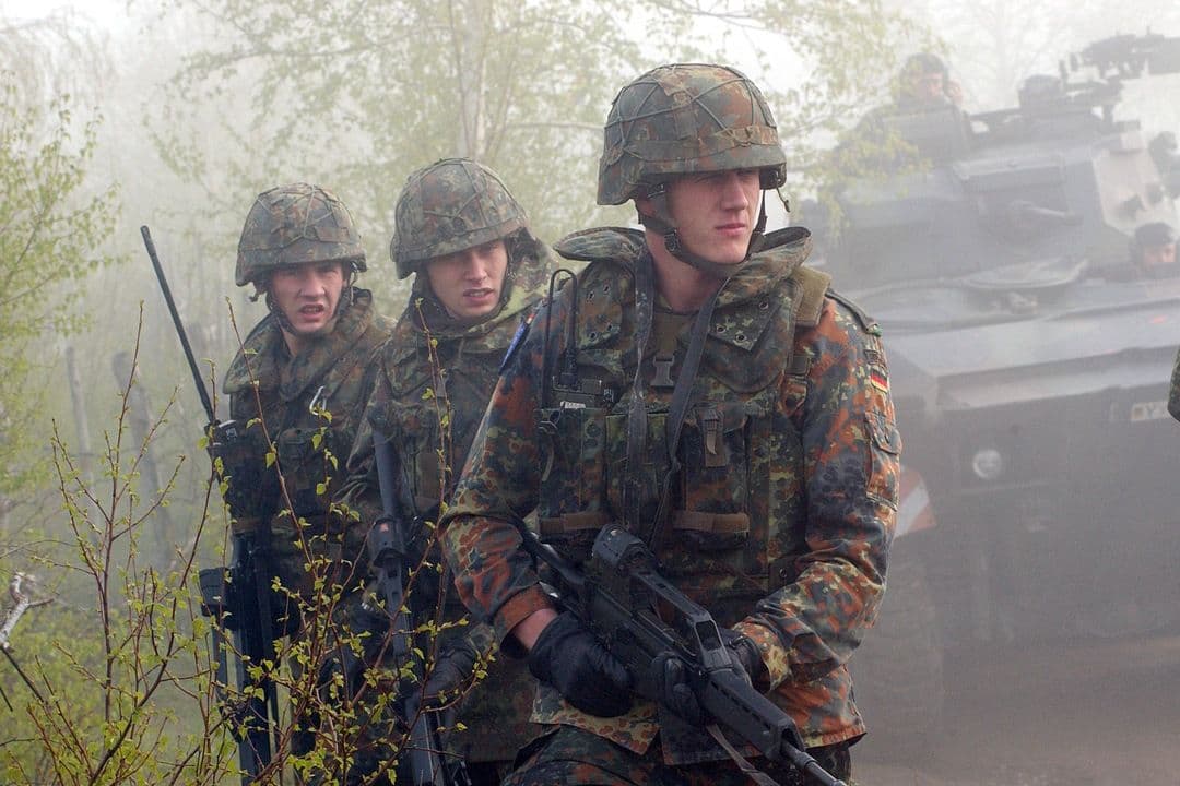 German soldiers with rifles advancing on foot through mist with armoured vehicle behind