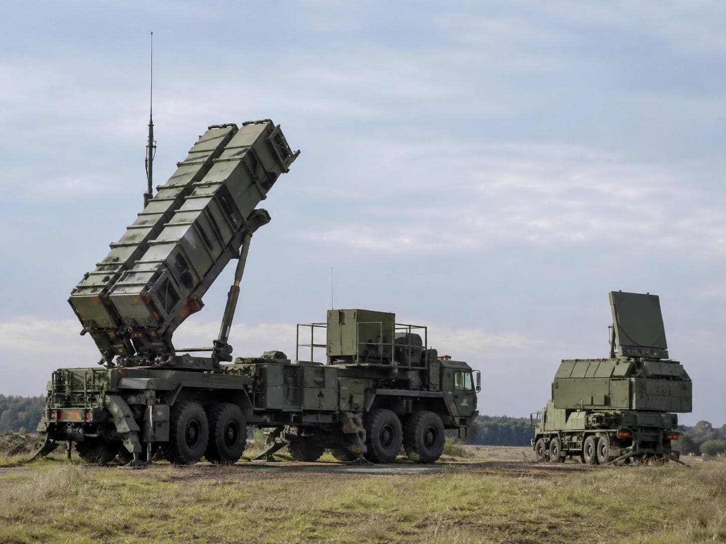 Patriot missile launcher with raised canisters beside a radar unit in an open field